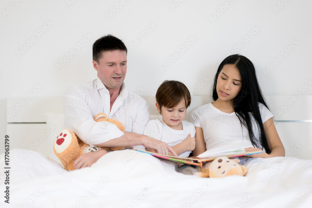 Asian child boy reading book together on bed in bedroom with father and mother. Happy family concept. Asian child boy reading book together on bed in bedroom with father and mother. Happy family concept.