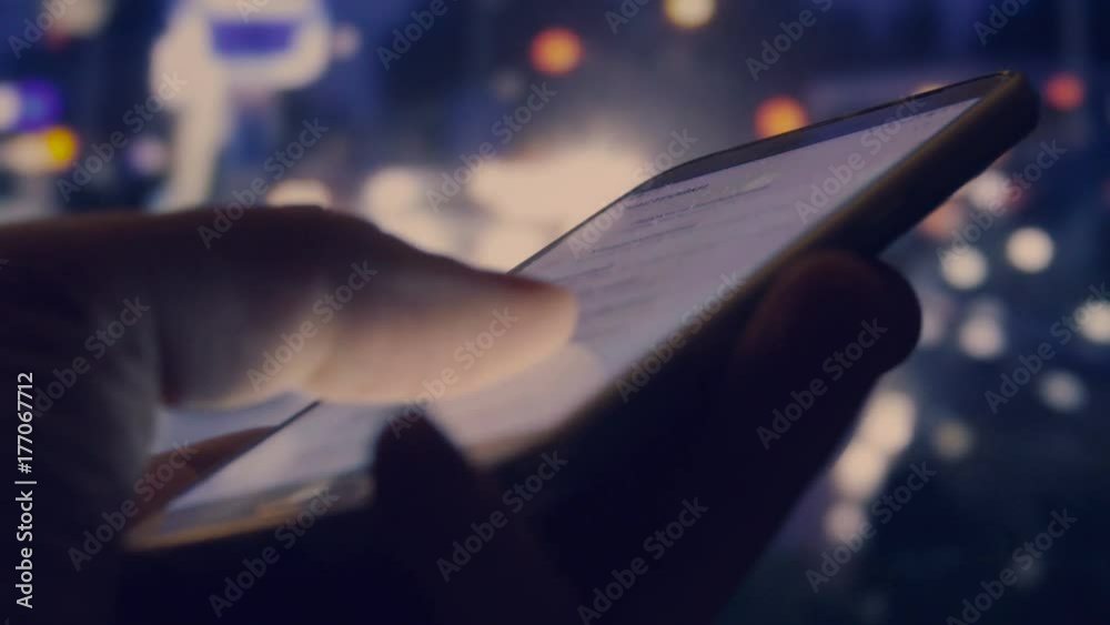 Close-up shot of male hand touching smartphone at night with blurred city lights on the background  
