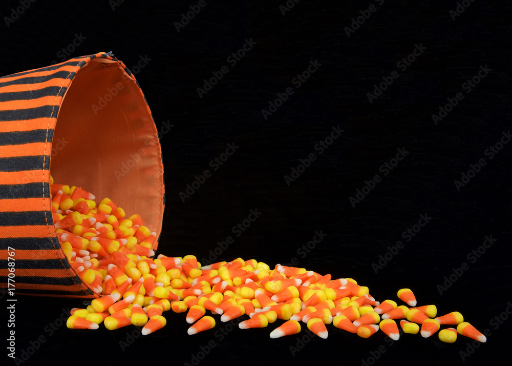 Obraz premium Candy corn traditional to Halloween spilling out of a black and orange bucket onto a black background with copy space