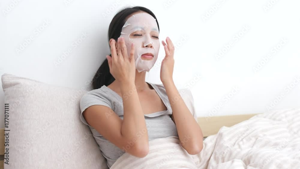 Woman applying facial mask and sitting on bed Woman applying facial mask and sitting on bed