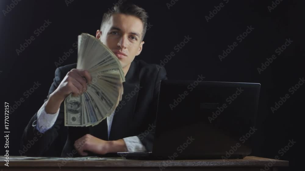 young successful businessman with dollar bills stacked in a fan working on a laptop young successful businessman with dollar bills stacked in a fan working on a laptop