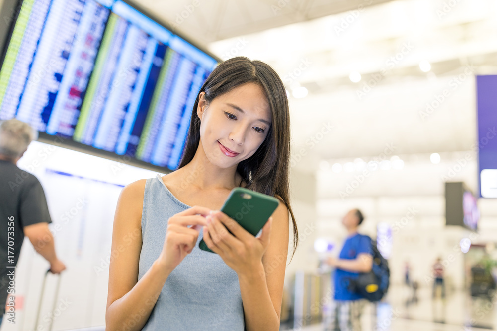 Woman checking flight number on the board and cellphone