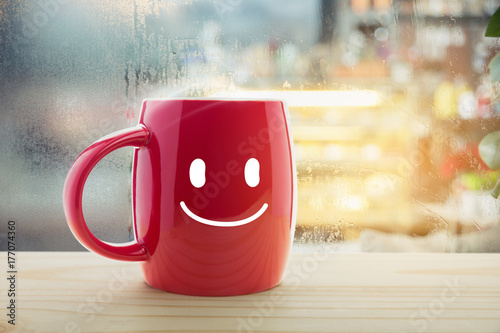 Red mug of coffee with a happy smile, Steaming red coffee cup on a rainy day window background, Good morning or have a happy day message concept