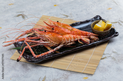 Grilled shrimps (Giant Tiger Pawn) with salt served with sliced lemon in black stone plate on makisu (Meal mat).