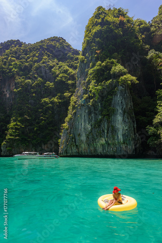 Lady with red hat on yellow pool float chic in beautiful crystal clear water at Pileh bay at Phi Phi island near Phuket, Thailand