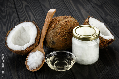Coconut, glass jar and wooden spoon with coconut oil on a wooden background.