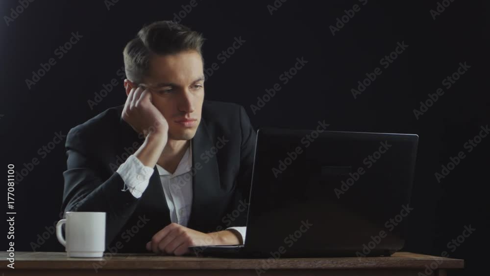 Bored businessman sitting by desk in dark office Bored businessman sitting by desk in dark office