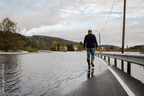 Man walking on the flooded road, water comes from the river Tovdalselva in Drangsholt in Kristiansand, Norway - October 3, 2017.