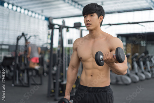 Fitness man in training showing exercises with dumbbells in gym