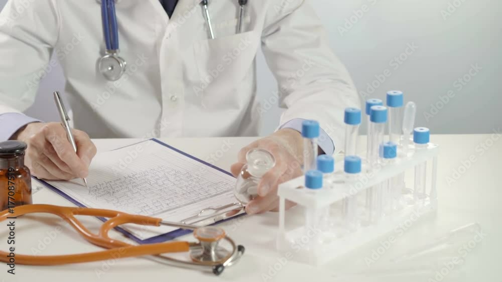Male doctor holding jar of pills and write prescription at worktable using silver pen Male doctor holding jar of pills and write prescription at worktable using silver pen