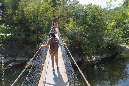 Young traveler girl and hikers goes through suspension bridge. Travel concept