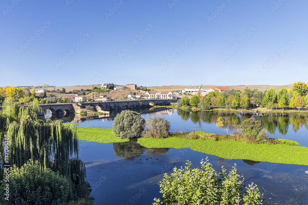 The Roman bridge over the Tormes river and its folliage in the ducal village of Alba de Tormes, Spain. Village were house the remains of Santa Teresa