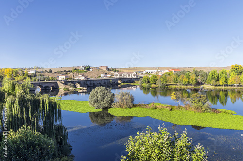 The Roman bridge over the Tormes river and its folliage in the ducal village of Alba de Tormes, Spain. Village were house the remains of Santa Teresa
