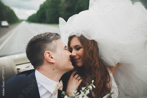 Stylish wedding couple, bride, groom kissing and hugging on retro car