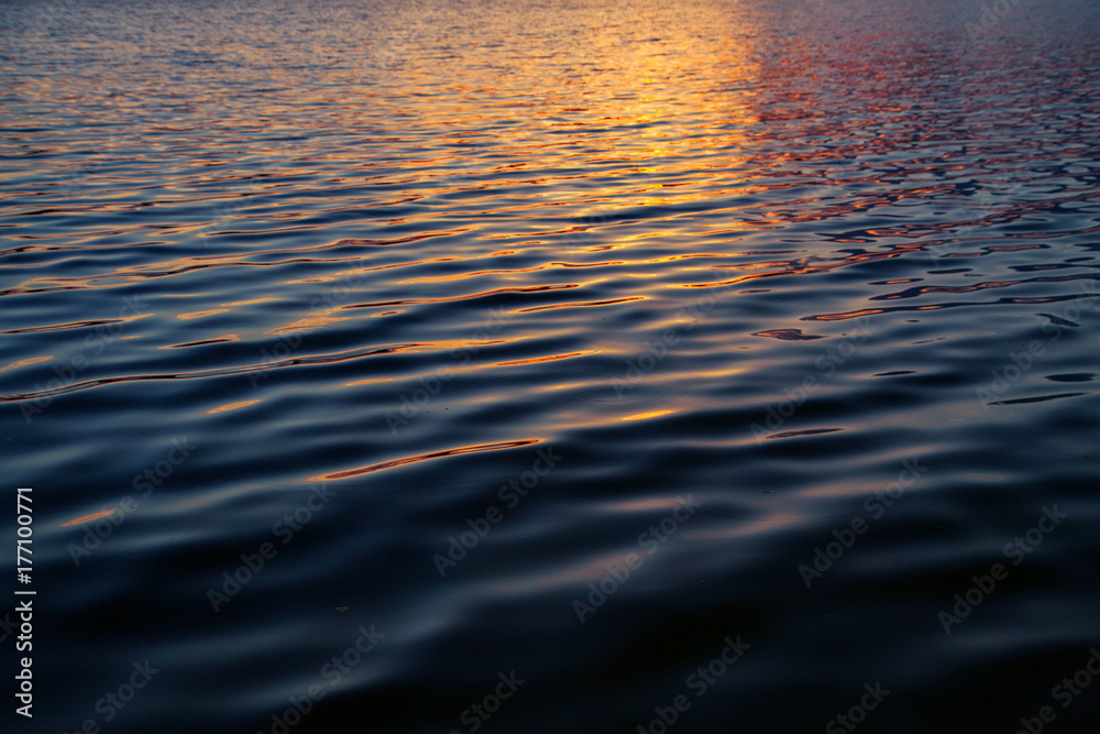 Texture of water. Sunset water with golden reflections. Dark water with small waves.