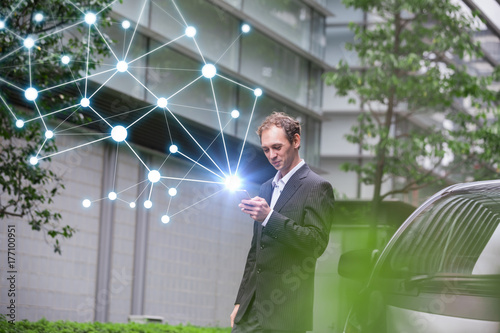 Middle aged businessman calling with smart phone beside of a car.