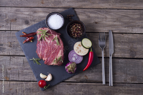 Raw meat steak from marble beef with vegetables and spices on the stone plate. Top view photo