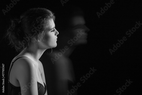 beautiful young woman and her blurred silhouette on black background with copy space, monochrome