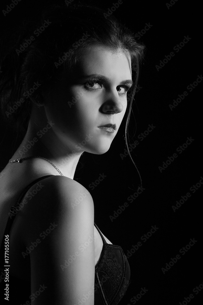 beautiful sad young woman on black background looking over shoulder at camera, monochrome