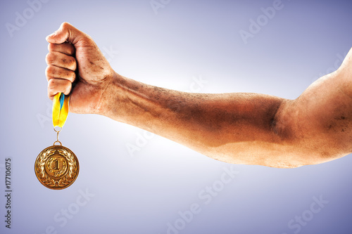 Man's hand is holding gold medal on a blue background.