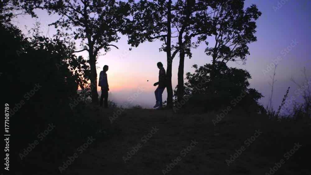 silhouettes of two tall slim guys playing footbag freestyle early in morning on hill over big city covered with fog in slow motion silhouettes of two tall slim guys playing footbag freestyle early in morning on hill over big city covered with fog in slow motion