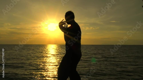 Man is practicing self-defence technique at the sea. Silhouette of a man on the background at sunset of the sea practicing martial arts. photo
