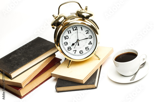 Reloj dorado despertador retro con libros apilados y taza de café sobre fondo blanco aislado. Vista de frente y superior