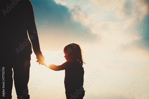 silhouette of little girl holding parent hand at sunset photo