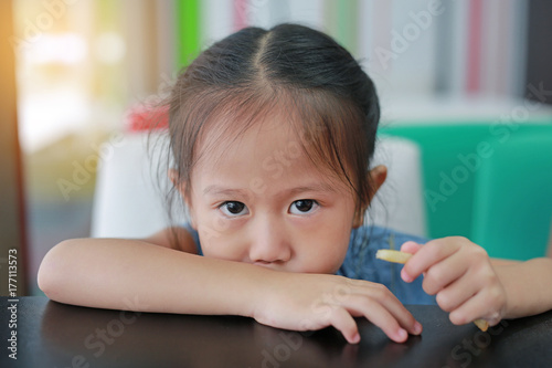 Little girl sitting at table and eating French fries.