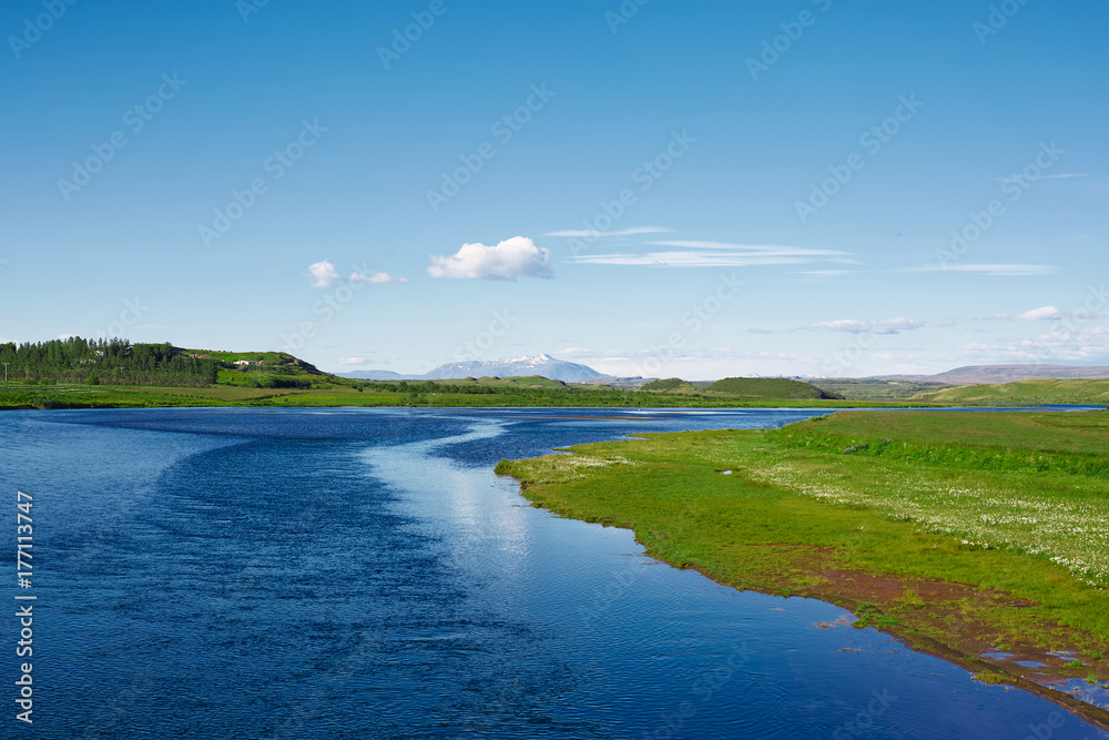 Icelandic scenery with salmon river, mountains in the background and blue sky. Summer vacation and travel to Iceland
