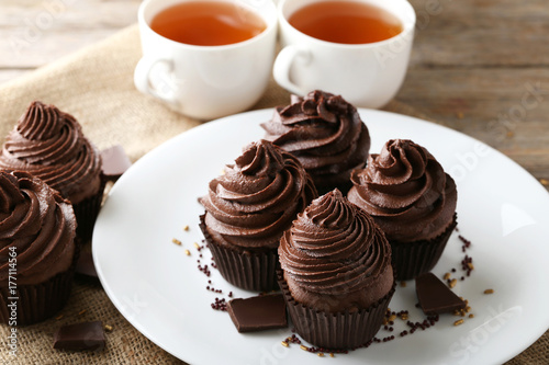 Chocolate cupcakes in plate with cups of tea on wooden table