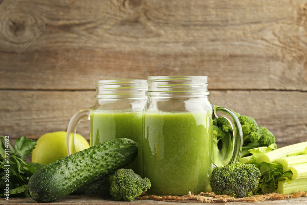 Bottles of juice with broccoli, celery and cucumber on grey wooden table Bottles of juice with broccoli, celery and cucumber on grey wooden table