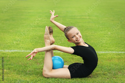Young girl gymnast with ball on green grass