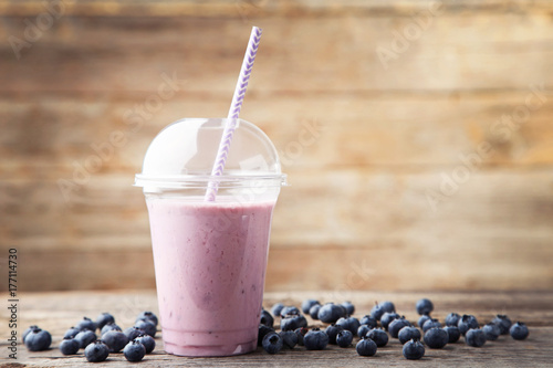 Sweet smoothie in plastic cup with blueberries on wooden table