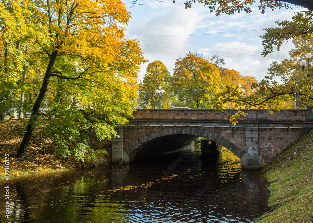 Old stone bridge crossing over the  city river canal. Yellow foliage in the autumn park. Riga, Latvia.
