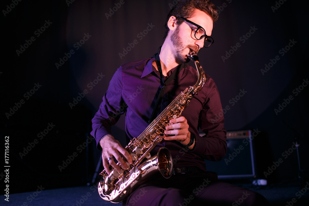 Naklejka premium Young saxophonist. Pink stage lightening