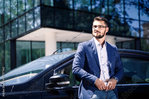 Young businessman standing near the car and holding phone