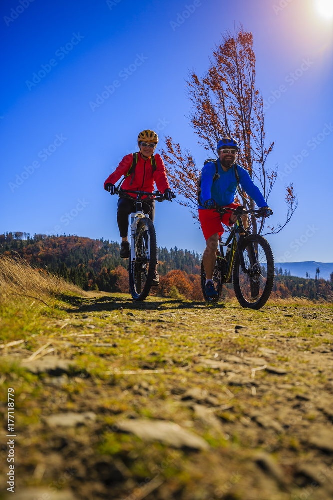 Fototapeta premium Cycling, mountain biker couple on cycle trail in autumn forest. Mountain biking in autumn landscape forest. Man and woman cycling MTB flow uphill trail.