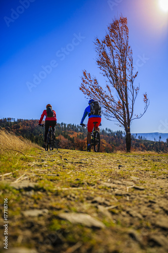 Kolarstwo, para rowerzystów górskich na szlaku rowerowym w lesie jesienią. Kolarstwo górskie w jesień krajobraz lasu. Mężczyzna i kobieta na rowerze MTB płyną pod górę szlaku.