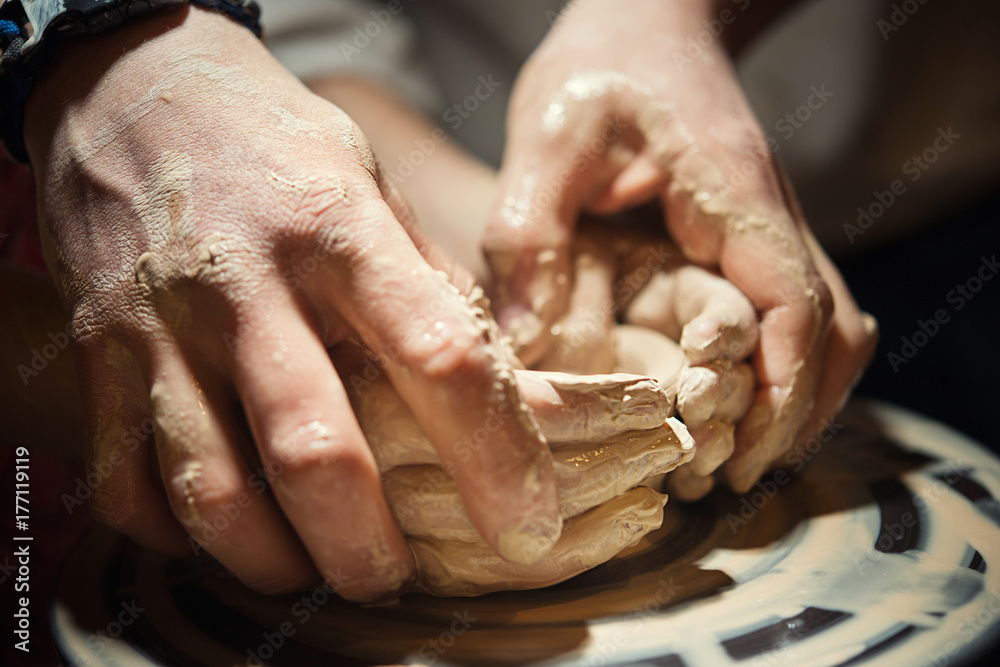 Teacher man teaches a child how to make a ceramic plate on the potter's pile. Close-up of child's hands and masters.