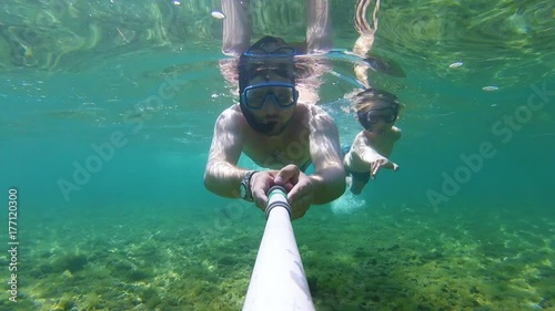 Father and son with fins, mask, snorkel and a selfie stick swimming in the sea, gopro underwater footage