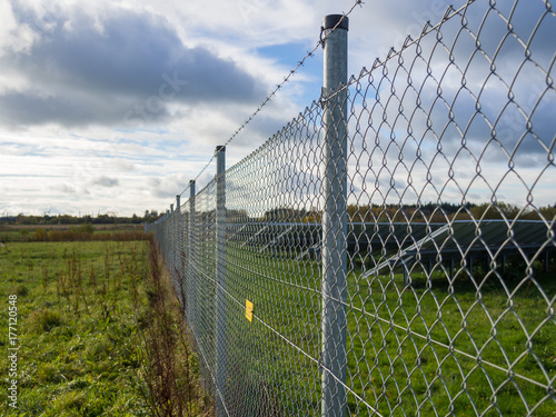 Long metal chainlink fence securing solar or photovoltaic panel farm with dramatic cloudy sky in North Germany