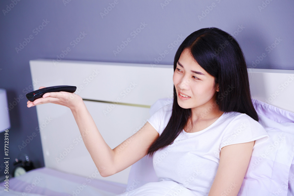 smilling woman with tv remote control on bed in bedroom smilling woman with tv remote control on bed in bedroom