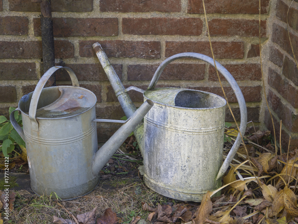 two old rusty tin watering can in cemetery wall two old rusty tin watering can in cemetery wall