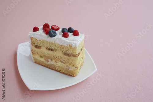 a piece of cake with blueberries and raspberries is on the table with a pink color