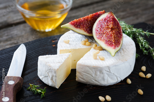 White cheese brie or camembert, figs, honey and nuts on dark cutting board. Closeup view
