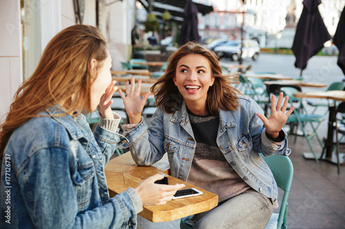 Two pretty brunette woman in keans casual wear having fun while sitting in city cafe photo