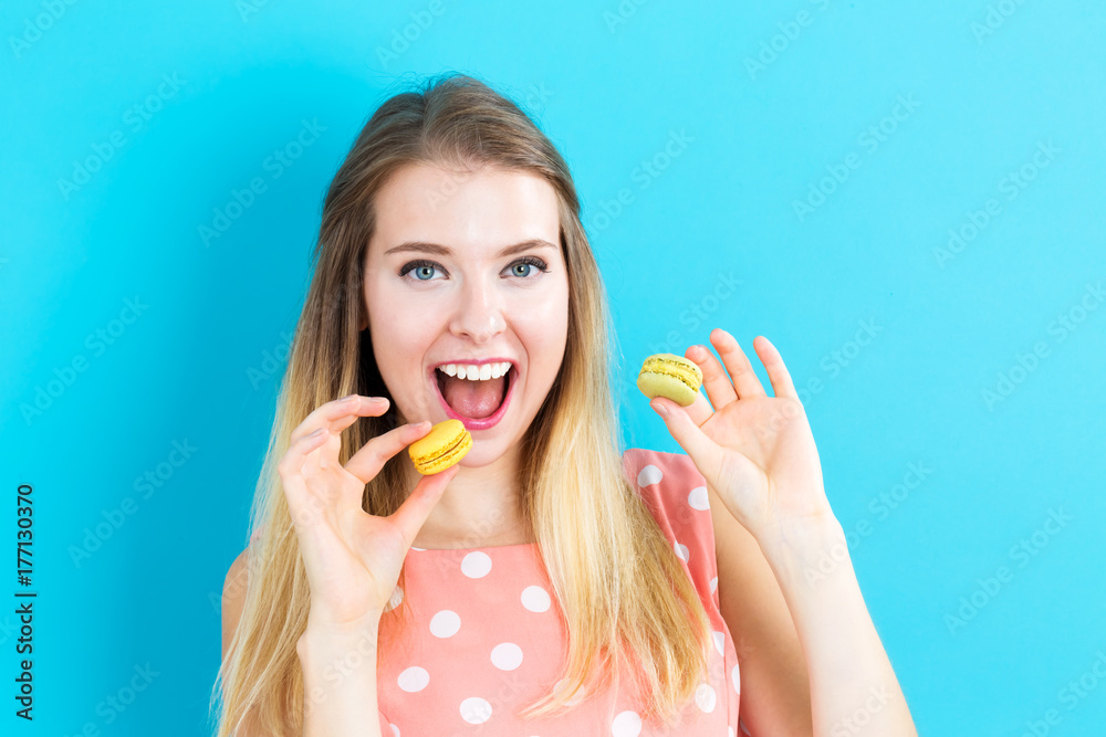 Happy young woman holding macarons on a blue background