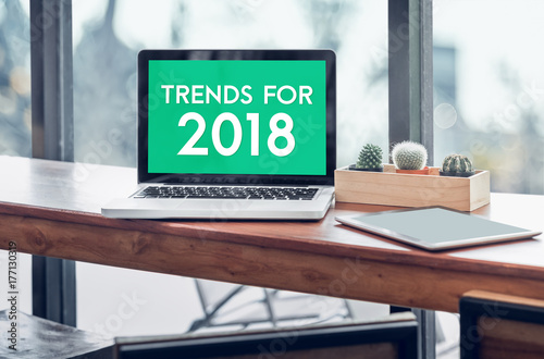 Trends for 2018 word in laptop computer screen with tablet on wood stood table in at window with blur background,Digital Business or marketing trending