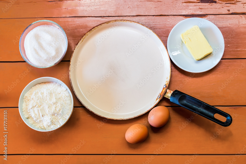 Eggs, butter, flour, sugar and frying pan on painted rustic wooden background. Eggs, butter, flour, sugar and frying pan on painted rustic wooden background.